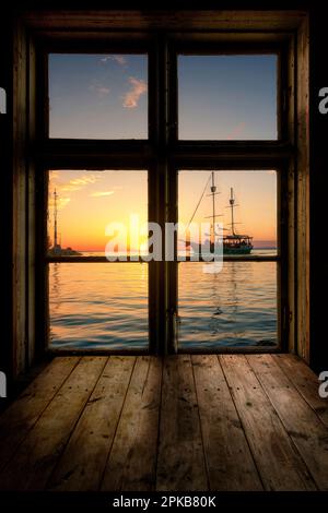 Blick aus einem Holzfenster auf den Balaton/Lake Balaton, Segelschiff bei Sonnenuntergang. Stockfoto