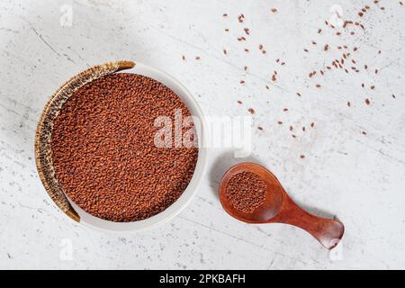 Kresse ( Lepidium sativum ) Samen in einer kleinen weißen Schüssel mit Holzlöffel, Blick von oben, einige auf einem steinähnlichen Schreibtisch Stockfoto