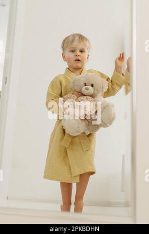 Porträt eines Jungen im Spiegel. Ein Junge im Bademantel umarmt einen Bären. Stockfoto