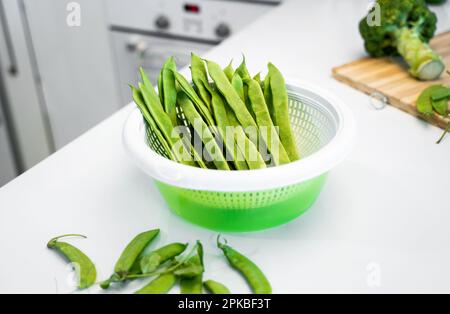 Grünes Gemüse, romano-Helda-Bohnen, grüne Erbsen und Brokkoli auf dem Holzbrett. Weißer Küchentisch zu Hause. Das Konzept einer gesunden Ernährung Stockfoto