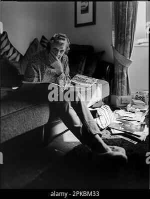 Schwarz-weiß-Bild einer älteren Frau, erschrocken und in die Kamera blickend, hat sie Rollers im Haar und liest Zeitungen Stockfoto