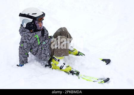 Ein glücklicher Skifahrer fiel, saß auf einer Piste in einem Schneesturm, in einem Skigebiet in den Alpen Stockfoto