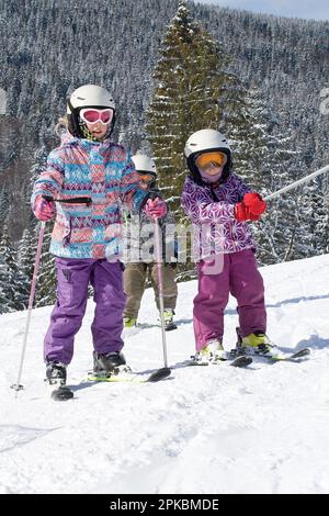 Dad fährt mit einem kleinen Tochter-Skifahrer auf einer Skipiste entlang einer sanften Piste in einem Skigebiet in den Alpen Stockfoto