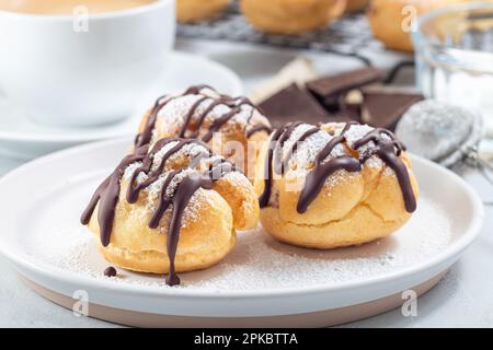 Hausgemachte Profiteroles mit Schlagsahne und Schokoladenfüllung, bedeckt mit geschmolzener Schokolade, auf einem Teller, horizontal Stockfoto