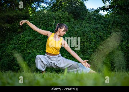 Junge Frau, die in der Natur Tai Chi Chuan praktiziert. Chinesische Managementfähigkeiten Qis Energie. Stockfoto