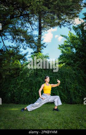 Eine Frau, die im Park Tai Chi Quan praktiziert. Tai Chi ist eine körperliche und geistige Praxis aus China, die sanfte, fließende Bewegungen mit verbindet Stockfoto