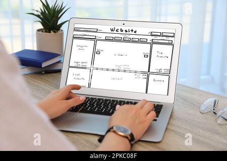 Designer erstellt Website auf Laptop am Holztisch, Nahaufnahme Stockfoto