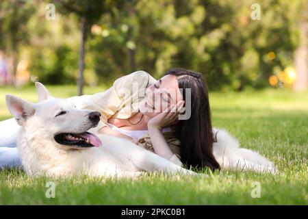 Teenager-Mädchen, die mit ihrem weißen Schweizer Schäferhund auf grünem Gras im Park liegt Stockfoto