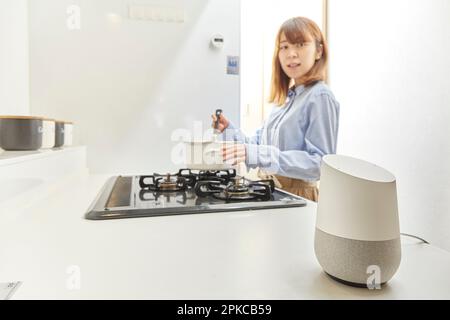 Frau, die mit dem AI-Lautsprecher spricht, während sie in der Küche kocht Stockfoto