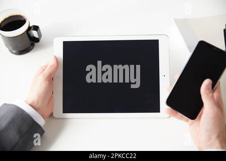 Geschäftsmann, der mehrere Geräte auf seinem Schreibtisch bedient Stockfoto