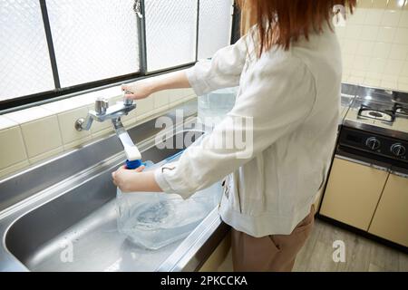 Eine Frau, die Wasser in einem einfachen Wasserkrug an einem Waschbecken füllt Stockfoto