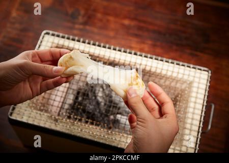 Eine Hand, die einen Reiskuchen auf einem Shichirin (einem traditionellen japanischen Kochherd) knackt und streckt Stockfoto