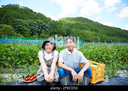 Mann und Frau mit Gemüse, die auf der Bank vor dem Feld sitzen Stockfoto