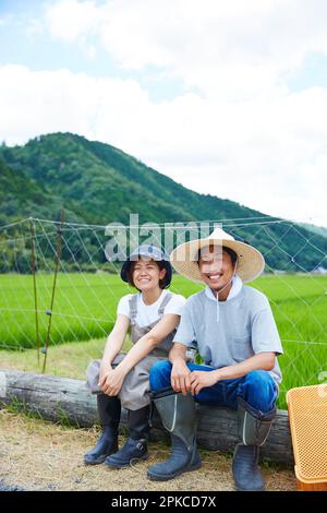 Lächelnde Männer und Frauen, die auf einem Baumstamm vor einem Reisfeld sitzen Stockfoto