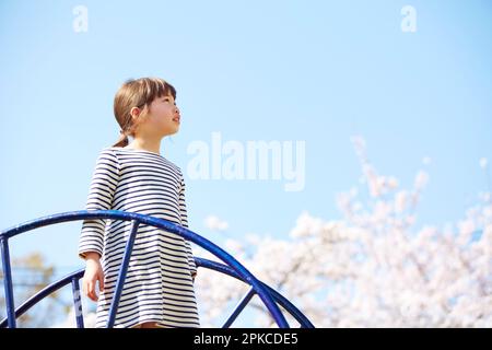 Ein Mädchen steht auf einer Rutsche in einem Park mit Kirschblüten Stockfoto