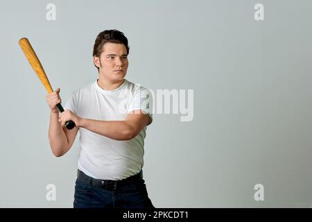 Ein Mann mit einem Schläger in der Hand schwingt auf grauem Hintergrund Stockfoto