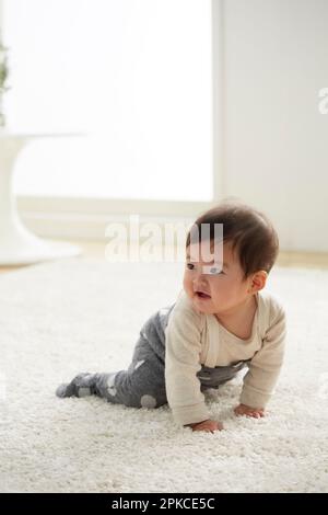 Baby krabbelt auf weißem Teppich Stockfoto