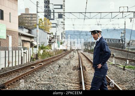 Mann in Arbeitskleidung und Helm, der die Gleise überquert Stockfoto