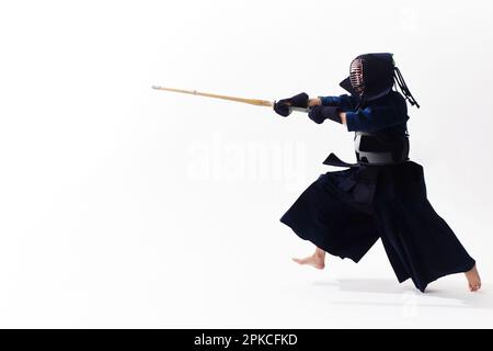 Ein Mann, der ein Kendo-Kleid trägt und einen Shinai nach unten schwingt Stockfoto