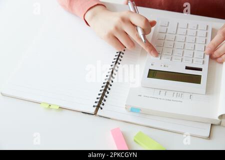 Frauenhand mit Taschenrechner auf einem offenen Notizbuch Stockfoto