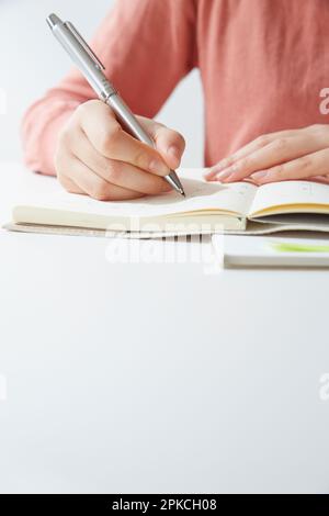 Die Hand einer Frau, die an ihrem Schreibtisch schreibt Stockfoto