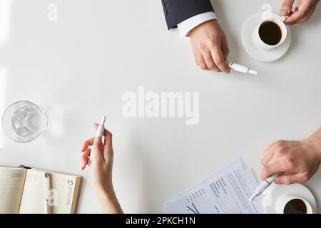 Zwei Männer in Anzügen mit E-Zigaretten in den Händen einer Frau und zwei Männer in Anzügen mit E-Zigaretten in den Händen von Frauen Stockfoto