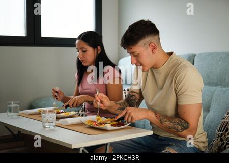 Zwei junge lateinamerikaner, die traditionelle Lappingachos essen, sitzen auf dem Sofa. Stockfoto