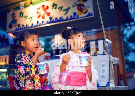 Ein Mädchen in Yukata isst rasiertes Eis von einem Festspielstand Stockfoto