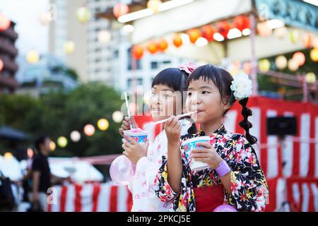 Ein Mädchen in Yukata isst rasiertes Eis vor der Yagura Stockfoto