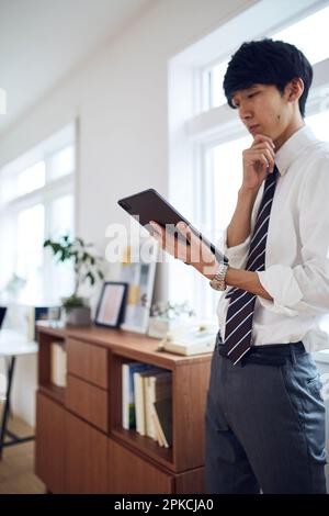 Ein Geschäftsmann, der sich in seinem Wohnzimmer um sein Tablet sorgt Stockfoto