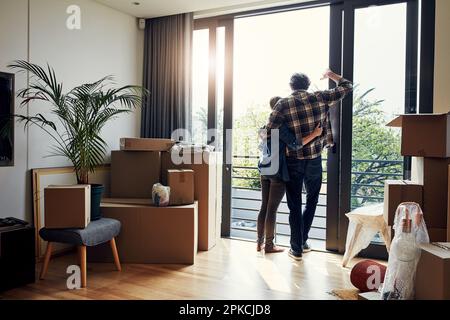 Wir haben es bis hierher geschafft. Rückansicht eines entspannten Paares mittleren Alters, das sich gegenseitig festhält, während es auf den Balkon in seinem neuen Zuhause schaut. Stockfoto
