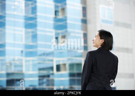 Rückansicht einer lächelnden Frau im Rekrutierungsanzug mit Gebäudehintergrund Stockfoto