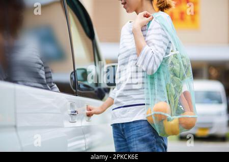 Eine Frau, die versucht, mit einem Öko-Sack in ein Auto zu steigen Stockfoto