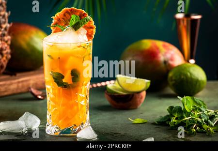 Alkoholischer Cocktail mit Wodka, Ananassaft, Mango, Likör, Eis. Longdrink oder sommerlicher kalter Mocktail. Tropischer dunkler Hintergrund mit Palmenblättern und Stockfoto