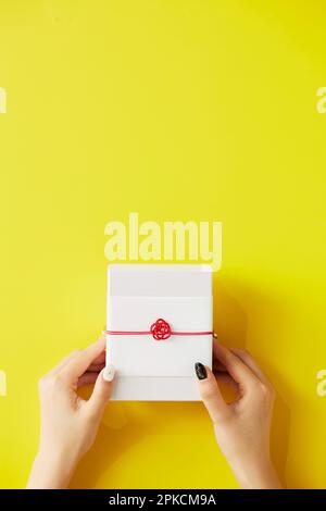 Geschenkbox mit Frauenhand auf gelbem Hintergrund Stockfoto