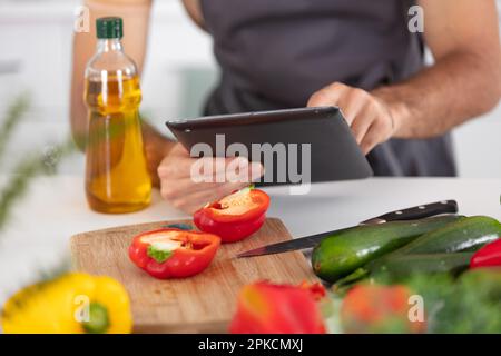 Zugeschnittene Ansicht eines Mannes, der Nahrung zubereitet und auf eine Tablette schaut Stockfoto