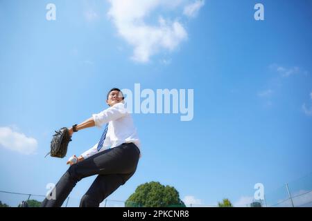 Ein Mann im Anzug, der unter blauem Himmel Baseball spielt Stockfoto