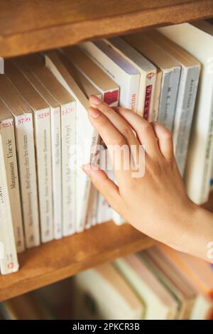 Die Hand einer Frau, die versucht, ein Buch im Bücherregal zu finden Stockfoto