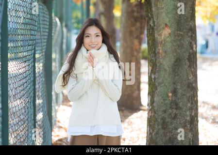 Eine Frau in ihren 20s Jahren läuft im Winter zwischen einem Drahtzaun und einem Baum in einem Park Stockfoto