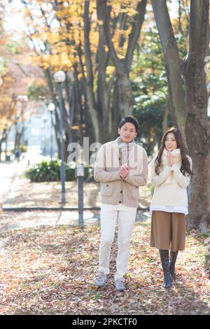 Ein Paar in den 20s Jahren, das im Spätherbst an einer von Bäumen gesäumten Straße entlang spaziert Stockfoto