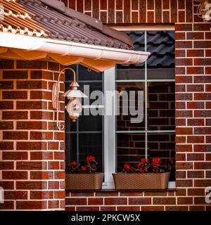 Ein Fenster mit Blumen eines privaten Backsteinhauses mit Blick auf den Hinterhof. Stockfoto