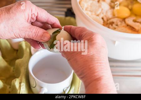 Gute bürgerliche Hausfrau kocht in der Küche, schlägt Eier und trennt Eigelb von weiß mit einer Tasse, um Brotklöße mit Semmelbröseln zu machen, Deutschland Stockfoto