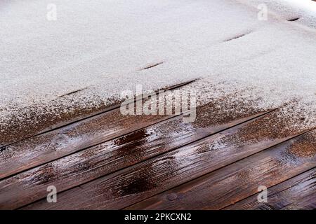 Schnee schmilzt auf dem Holzboden der offenen Veranda eines Privathauses. Stockfoto