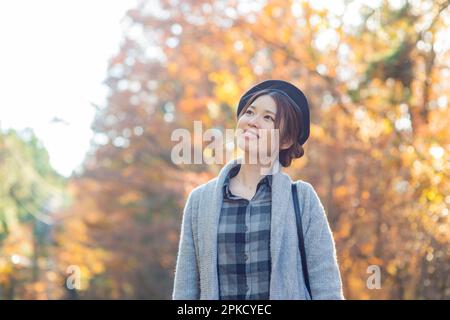 Eine Frau, die an einem Ort spaziert, während sie Herbstblätter sieht Stockfoto