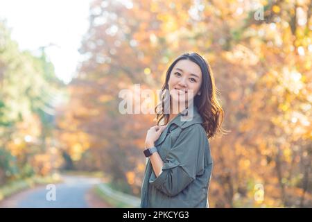 Eine Frau, die an einem Ort spaziert, während sie Herbstblätter sieht Stockfoto