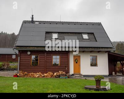 Sonnenkollektor auf schwarzem Dach mit kleinen Dachfenstern gegen bewölkten Himmel. Dunkler Regentag. Stockfoto