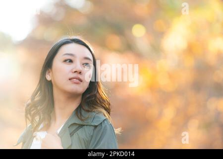 Eine Frau, die an einem Ort spaziert, während sie Herbstblätter sieht Stockfoto