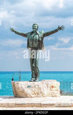 Bronzestatue des italienischen Sängers Domenico Modugno mit Blick auf die Altstadt auf den felsigen Klippen und dem blauen Meer mit offenen Armen wie dem berühmten Lied Volare Stockfoto