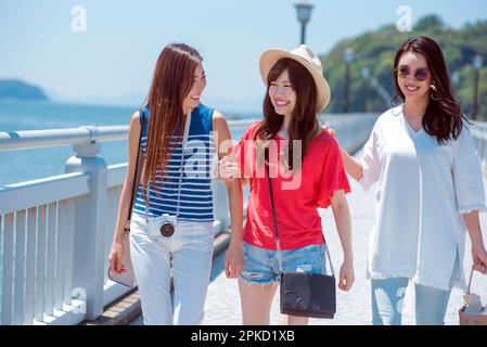 3 Frauen reisen in ein Resort, wo sie auf einer Brücke über das Meer gehen Stockfoto