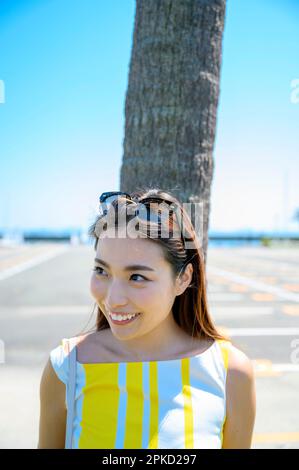 Eine Frau, die in ein Seebad reist und sich gegen eine Palme lehnt Stockfoto